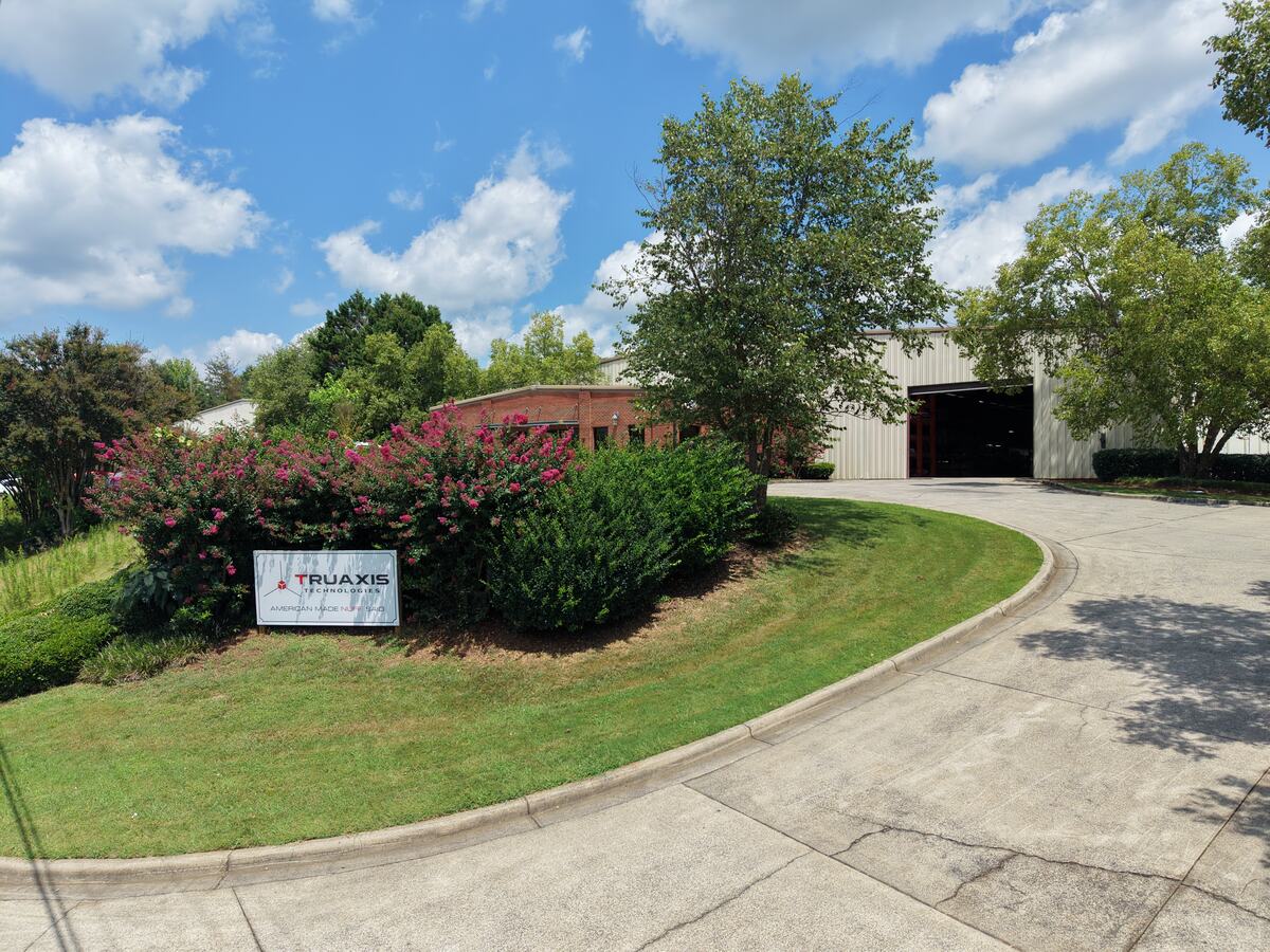 The TruAxis Technologies facility in Cartersville, Georgia, with the company sign at the driveway entrance and an open shop door.